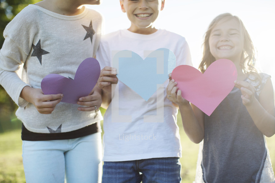 children holding paper hearts outdoors 