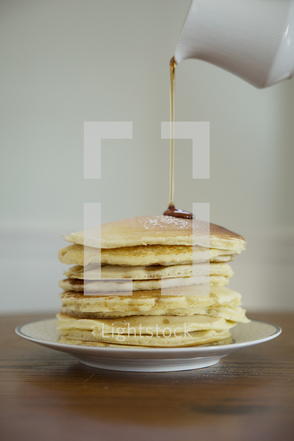 pouring syrup on a stack of pancakes 