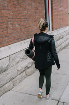 woman walking carrying a yoga mat 