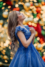 Woman looking up and praying surrounded with a bokeh of Christmas Lights