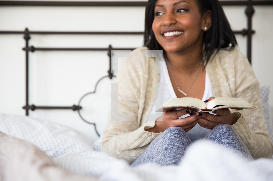 young woman sitting in bed reading a book