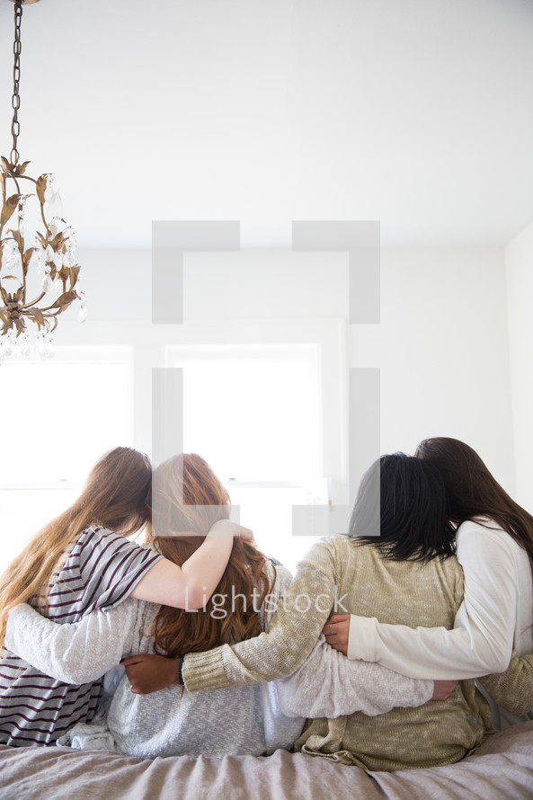 young women sitting on a bed talking and hugging