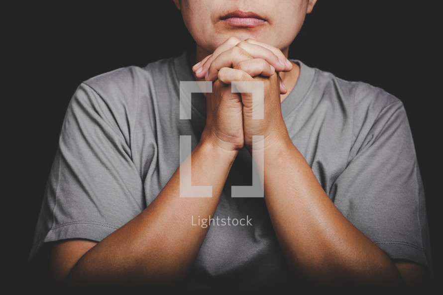 Woman in gray t-shirt praying with folded hands