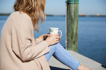 a woman with a coffee cup sitting on a pier 