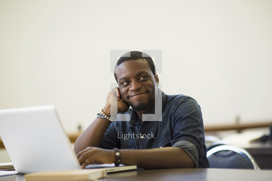 a smiling man sitting at a desk in front of a computer 