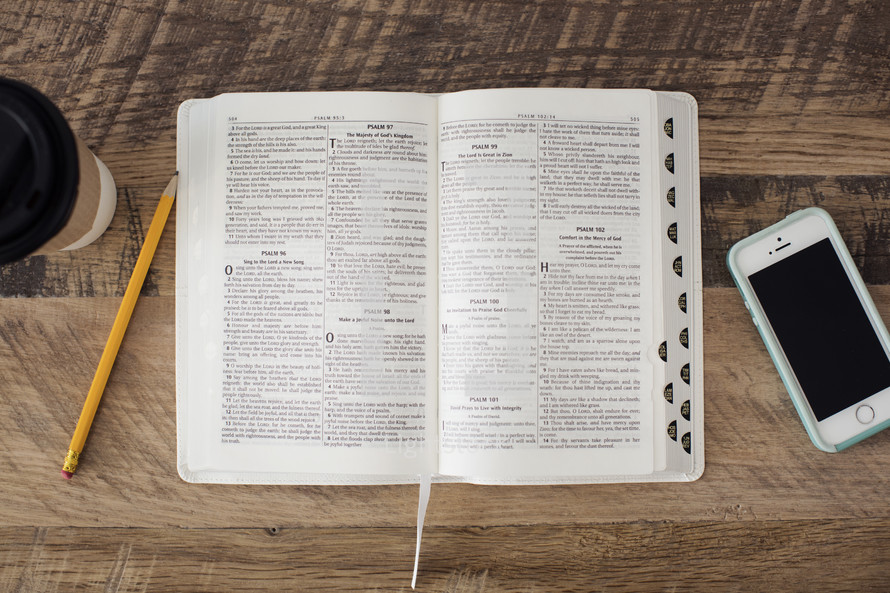 coffee cup, pencil, open Bible, and cellphone on a desk 