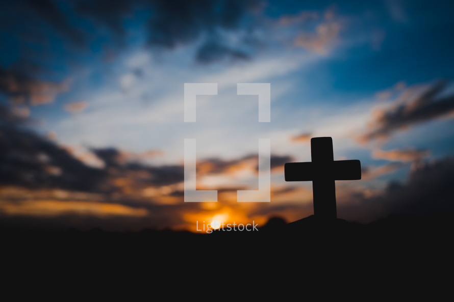 silhouette of a hand holding up a small cross at sunset 