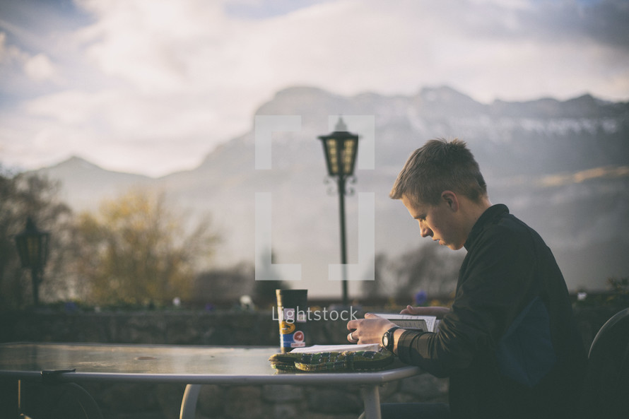 a man reading a Bible at an outdoor table 