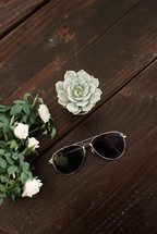 sunglasses, roses, and house plant on a wood countertop 