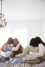 young women sitting on a bed talking and hugging