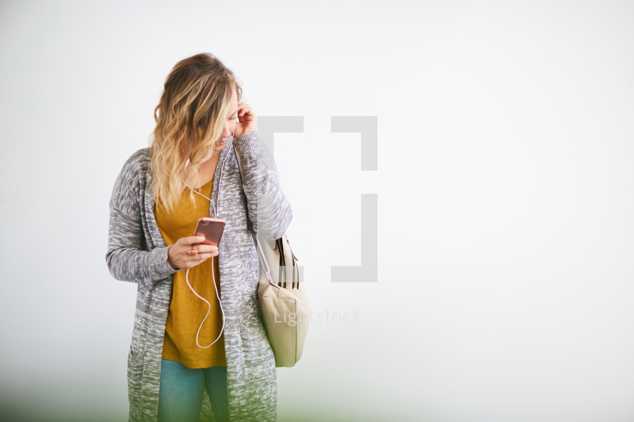 a woman standing holding a purse and listening to earbuds 