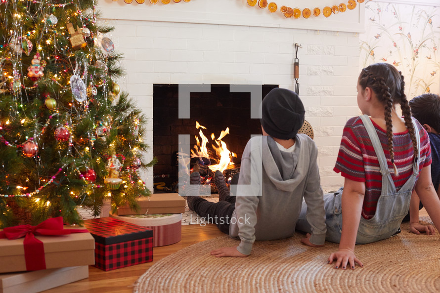 siblings sitting in front of a fireplace Christmas morning 