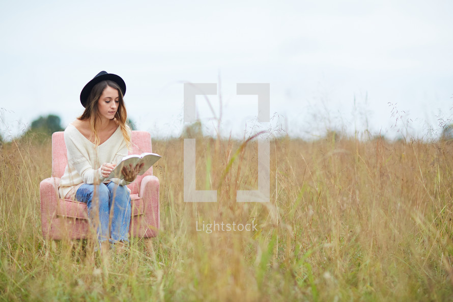 a woman sitting in a chair in a field reading a Bible 
