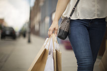 a woman walking down a sidewalk carrying shopping bags 