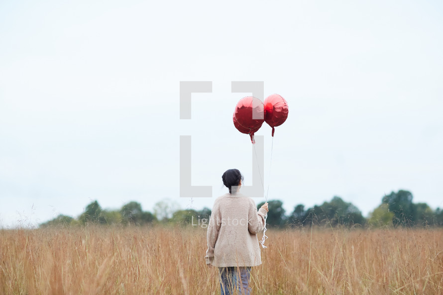 woman walking through a field carrying balloons 