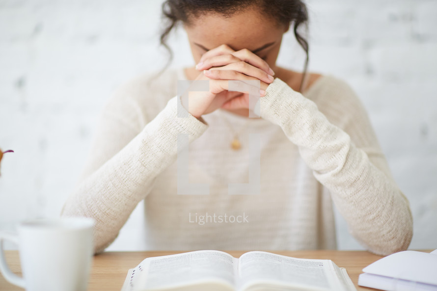 woman sitting at a desk praying over a Bible 