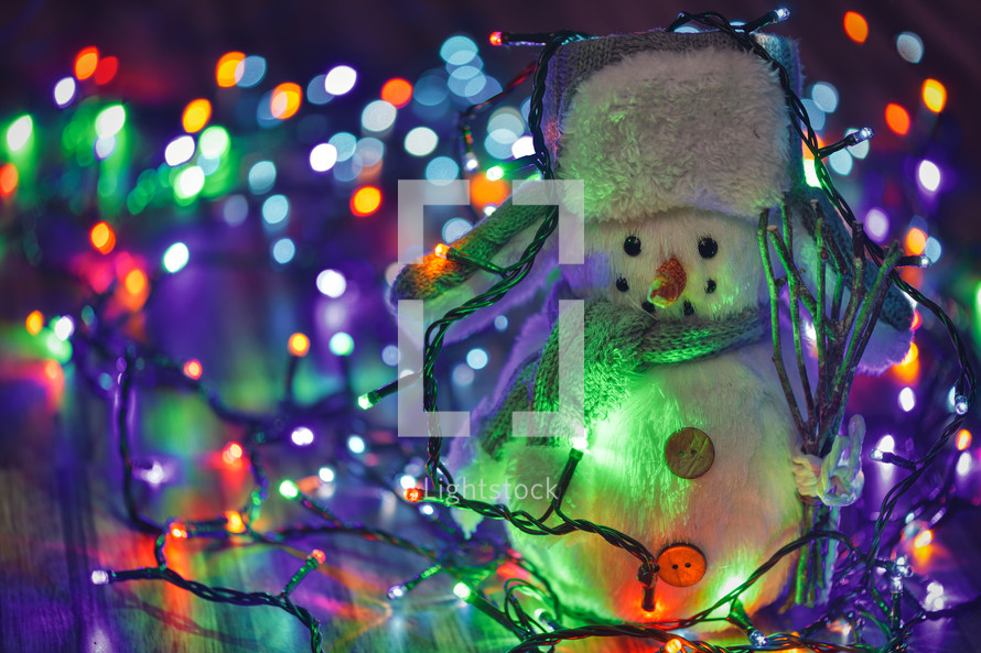 Small toy snowman on colorful Christmas lights background