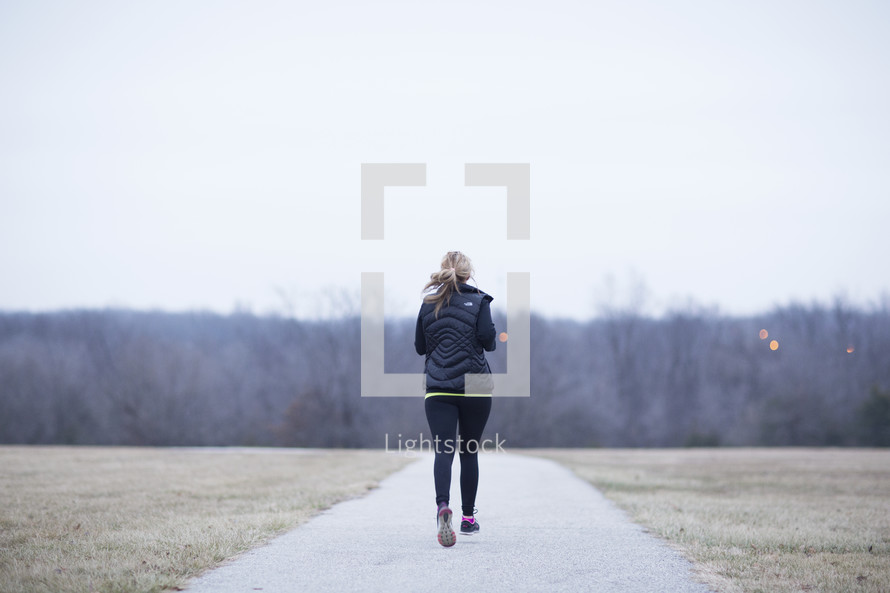 A woman jogging along a path in an open field.