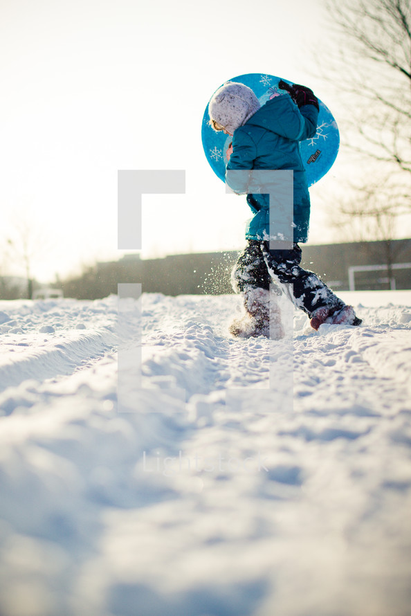 child carrying a sled through the snow