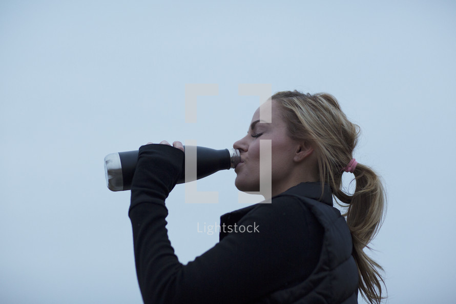 A woman drinking water from a stainless steel water bottle.