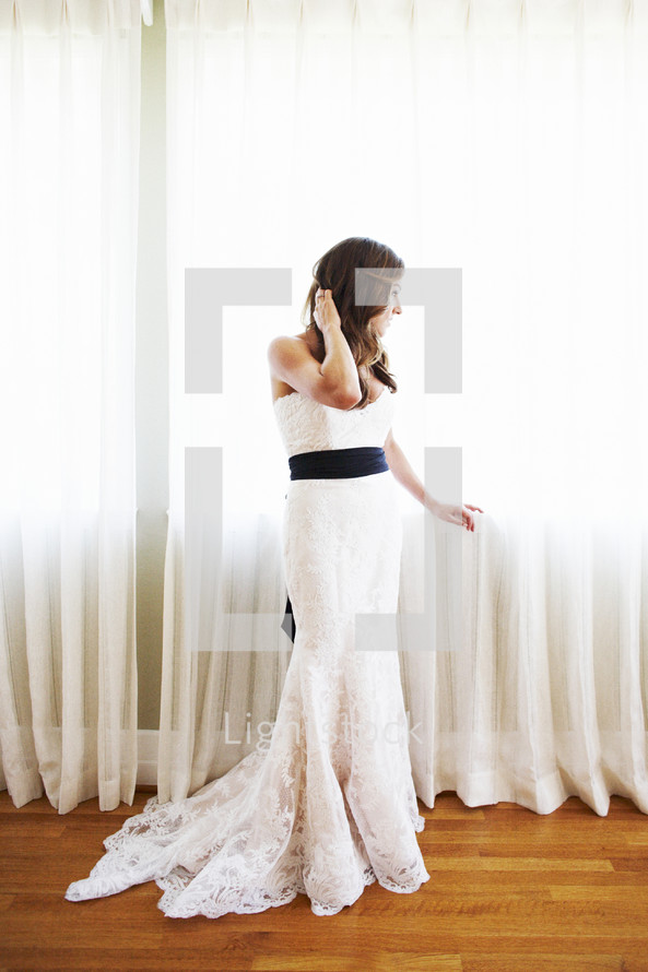 bride standing in front of a window draped with white curtains 