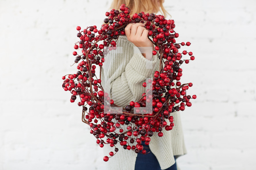 a woman standing with a red berry Christmas wreath 