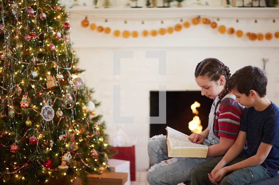 children reading a Bible around a Christmas tree 