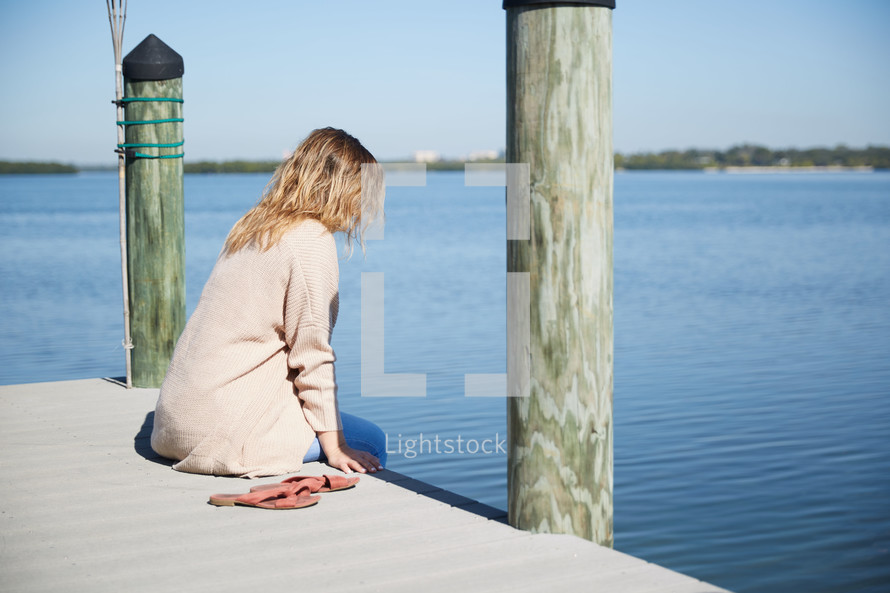 a woman sitting on a pier thinking 