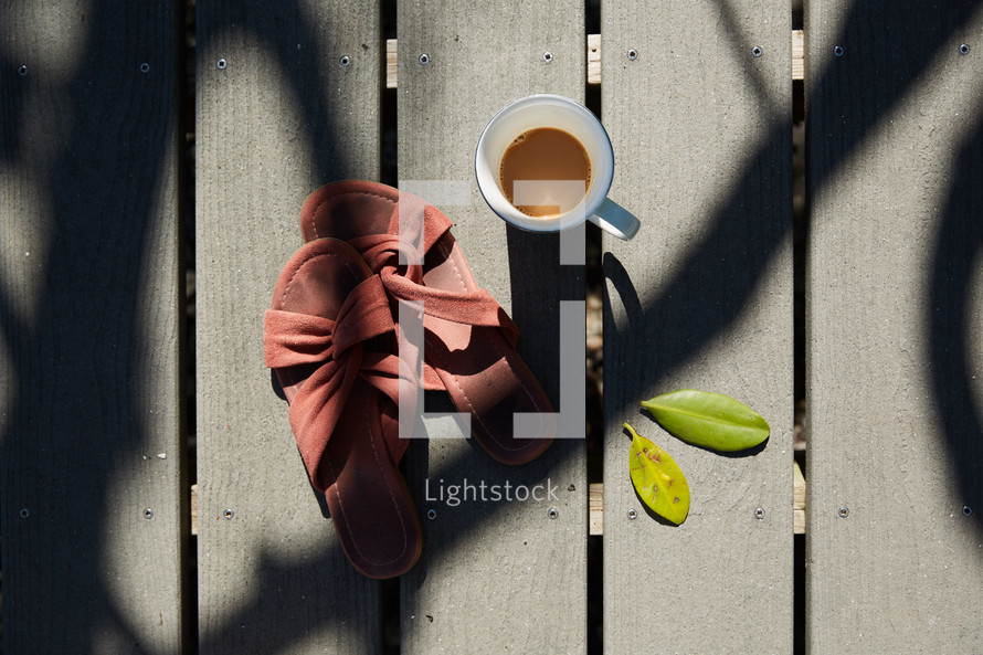 looking down at a coffee cup and sandals on a pier 