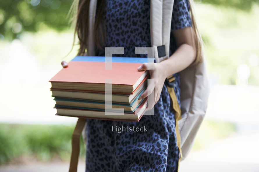a young girl holding books walking to school 