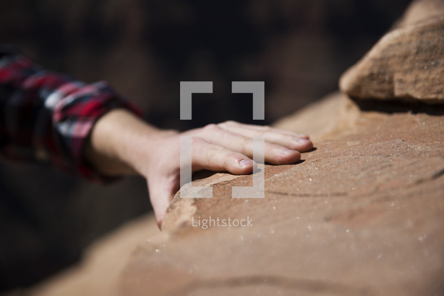 hand reaching to grab hold of a rock 