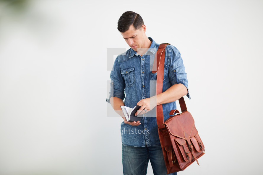 a man standing with a messenger bag reading a Bible 