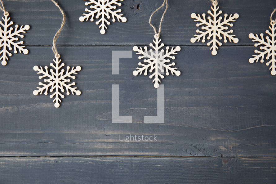 snowflake ornament border hanging on a wooden background.