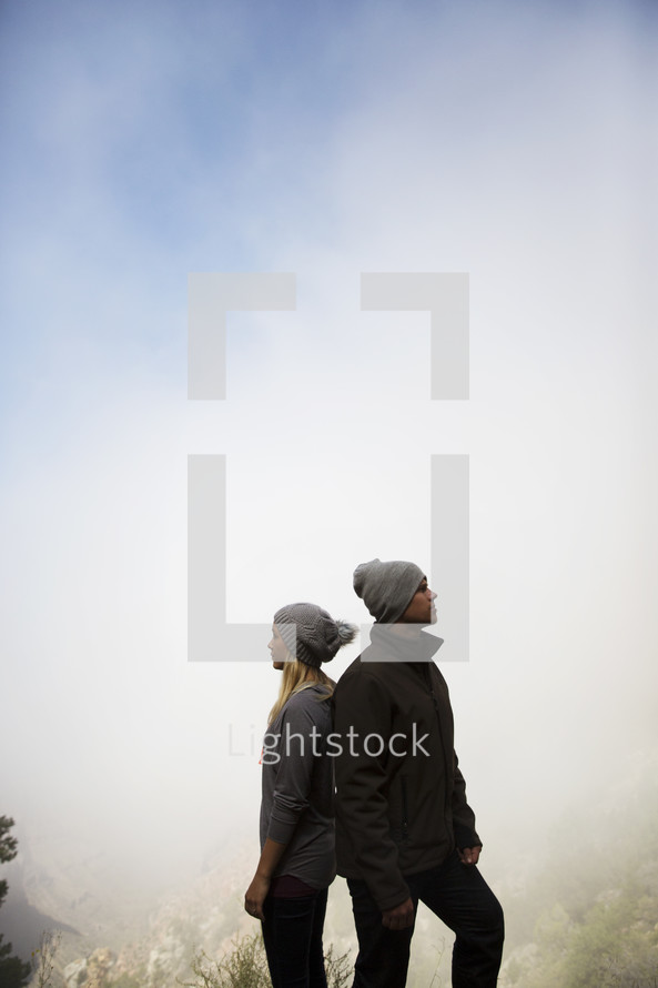 couple standing on a foggy mountaintop standing back to back 