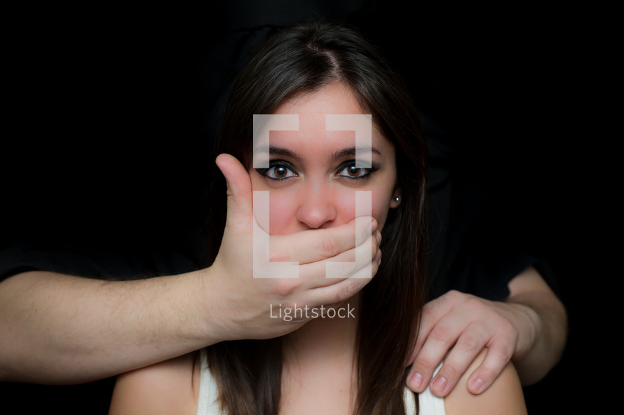 Hear no evil; speak no evil. A woman with her mouth and ear covered by a man's hands.