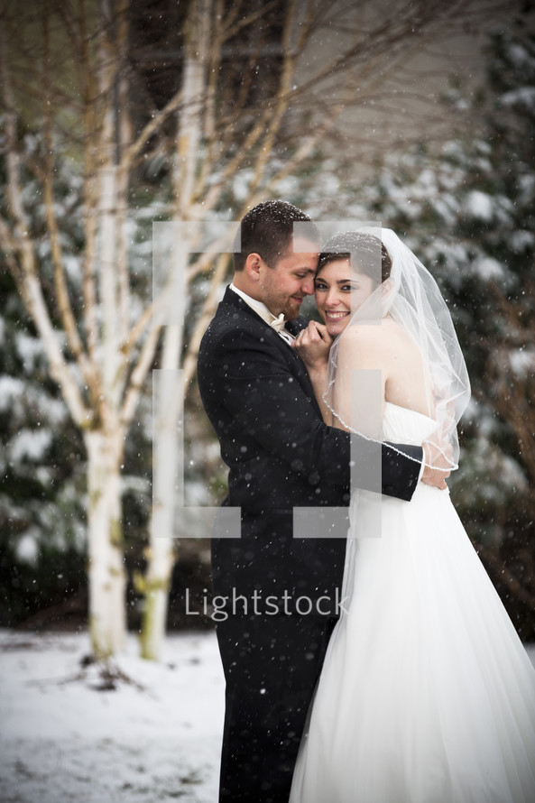 bride and groom hugging under falling snow