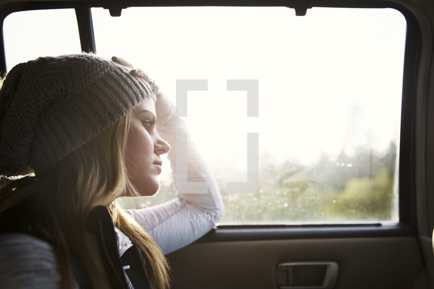 young woman looking out a car window in thought.