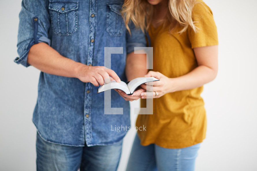 a man and woman standing reading the Bible together 