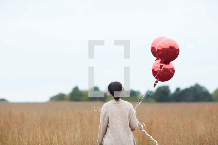 woman walking through a field carrying balloons 