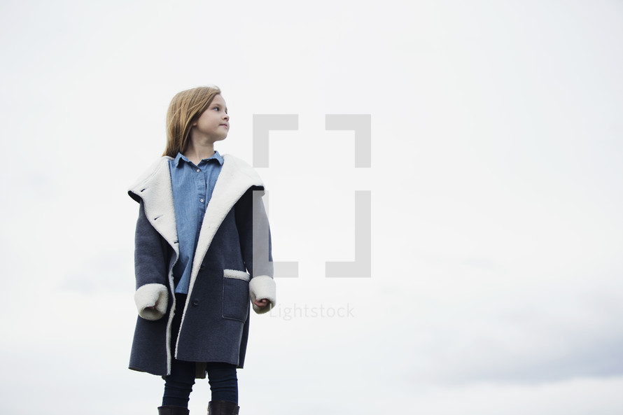 a child in a coat standing alone outdoors 