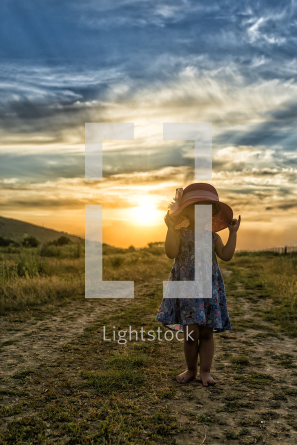 little girl in a hat at sunset on a dirt road 