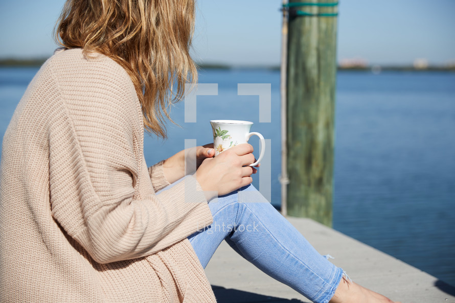 a woman with a coffee cup sitting on a pier 