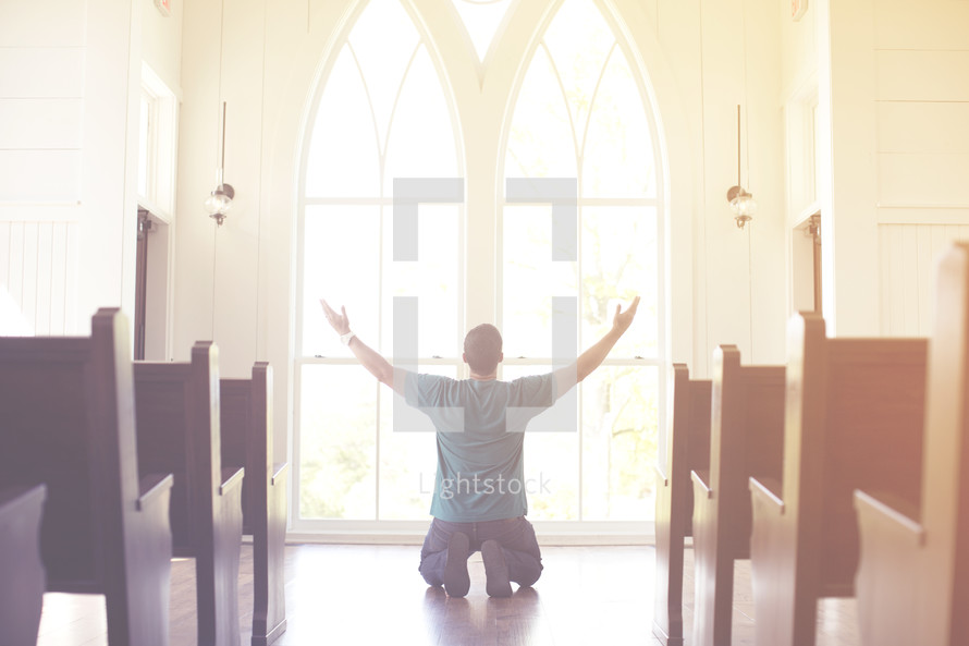 a man kneeling with his hands raised in worship at church