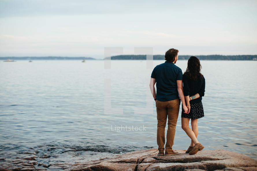 a couple standing on rocks along a shore 