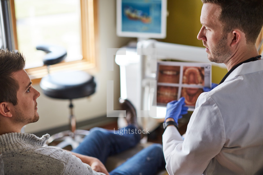 a dentist looking at digital scans of teeth and talking to his patient 