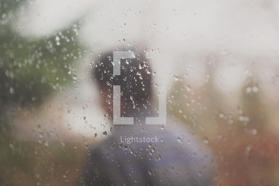 a young man walks away outside window with water drops