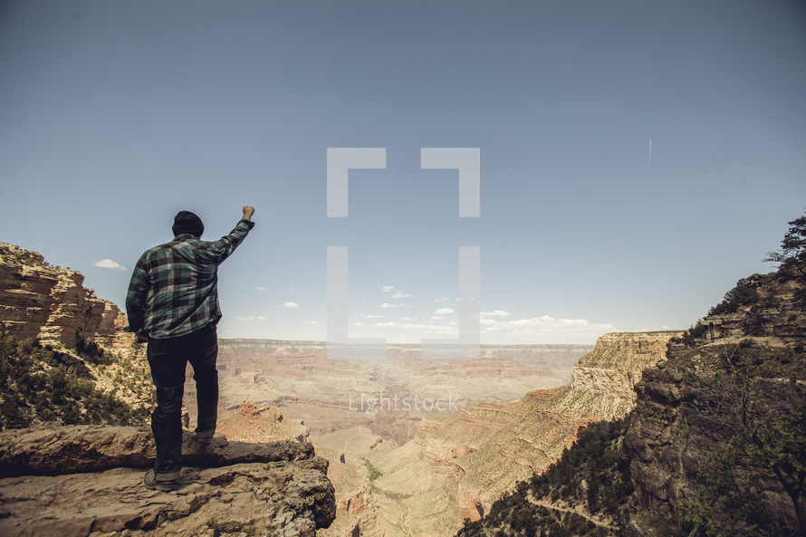 man standing with his fist in the air looking out over the Grand Canyon