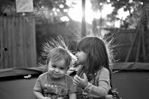 children sitting on a trampoline with static in their hair 
