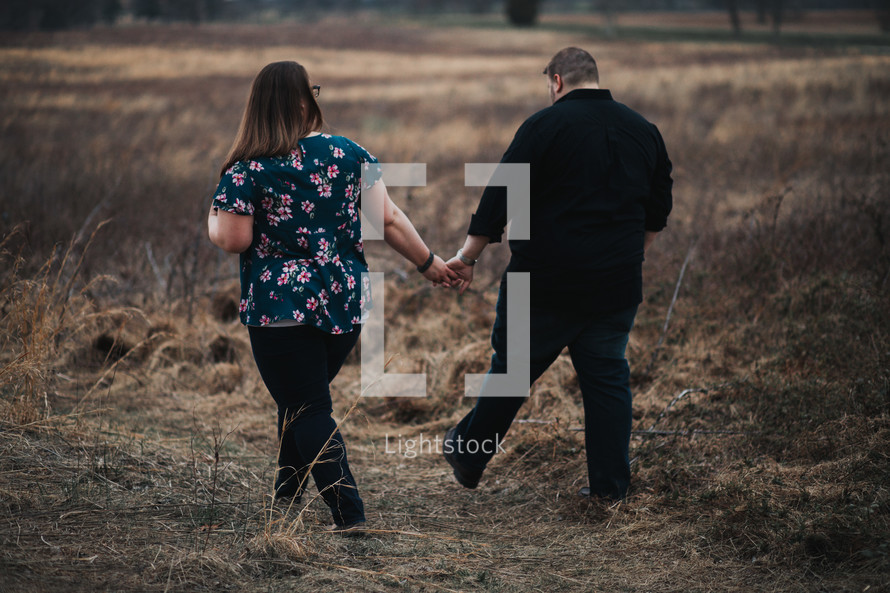 a couple walking through a brown field 