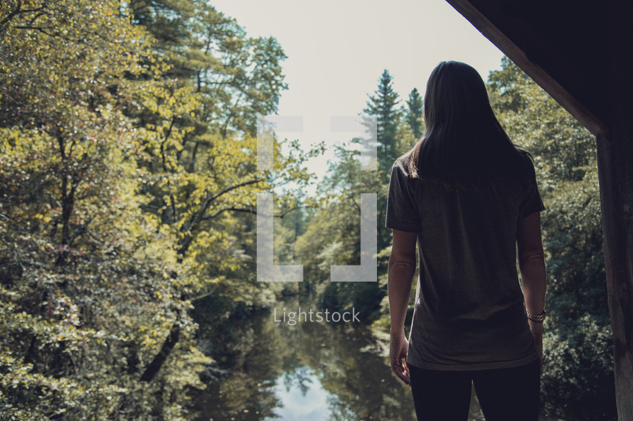 woman standing on a bridge looking out at a river 